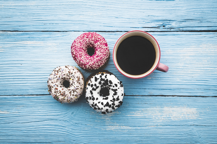 Coffee cup and colorful donuts on wooden blue background. Top View