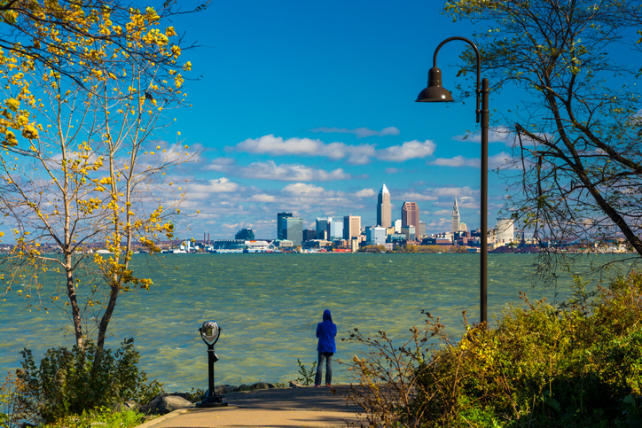 A woman wearing a hood looks at the Cleveland Skyline from a park just beside Lake Erie"n